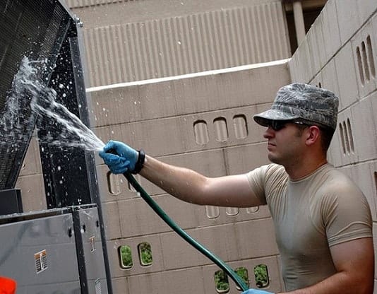 a man holding a green hose cleaning the Window Air Conditioning Unit