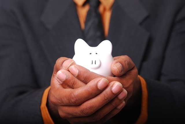 Two brown hands holding a white piggy bank