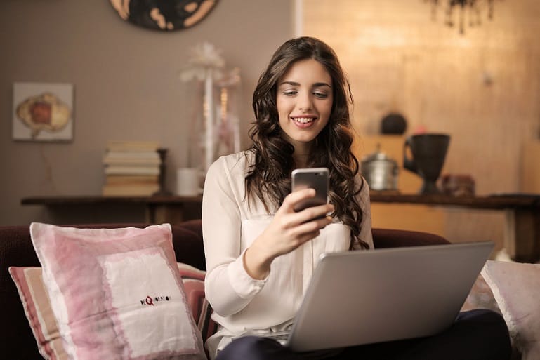 A woman sitting on the sofa holding a phone and a laptop on her lap relates to home energy audit