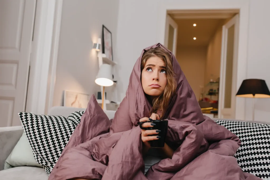 A cold, pouting girl wrapped in a purple blanket, illustrating the discomfort of a furnace blowing cold air.