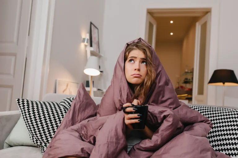 A cold, pouting girl wrapped in a purple blanket, illustrating the discomfort of a furnace blowing cold air.