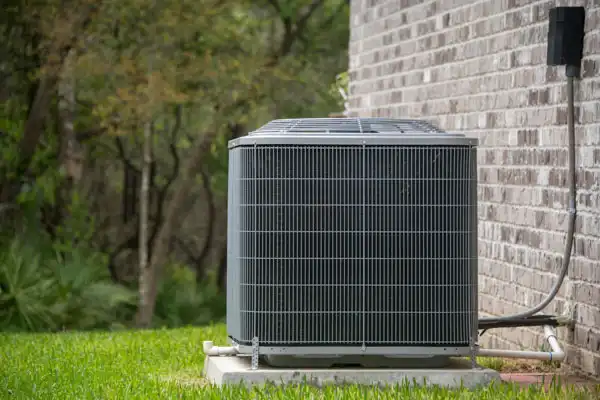 A reliable outdoor AC unit stands ready on a concrete pad by a brick building, showcasing All Hours Air’s expert 24/7 HVAC service.